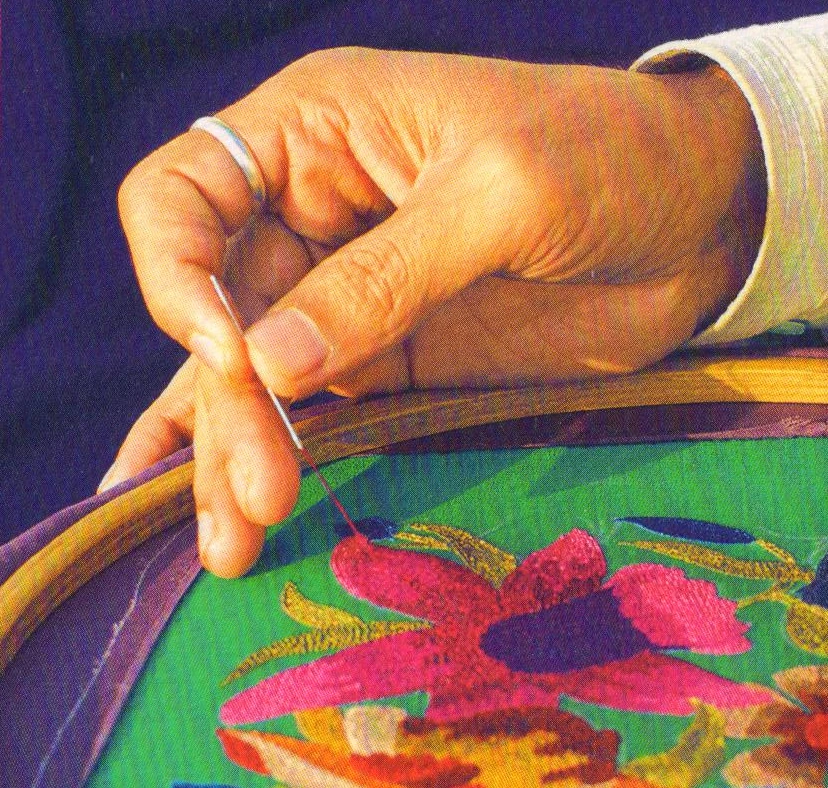 An artisan’s hand embroidering silk on a frame