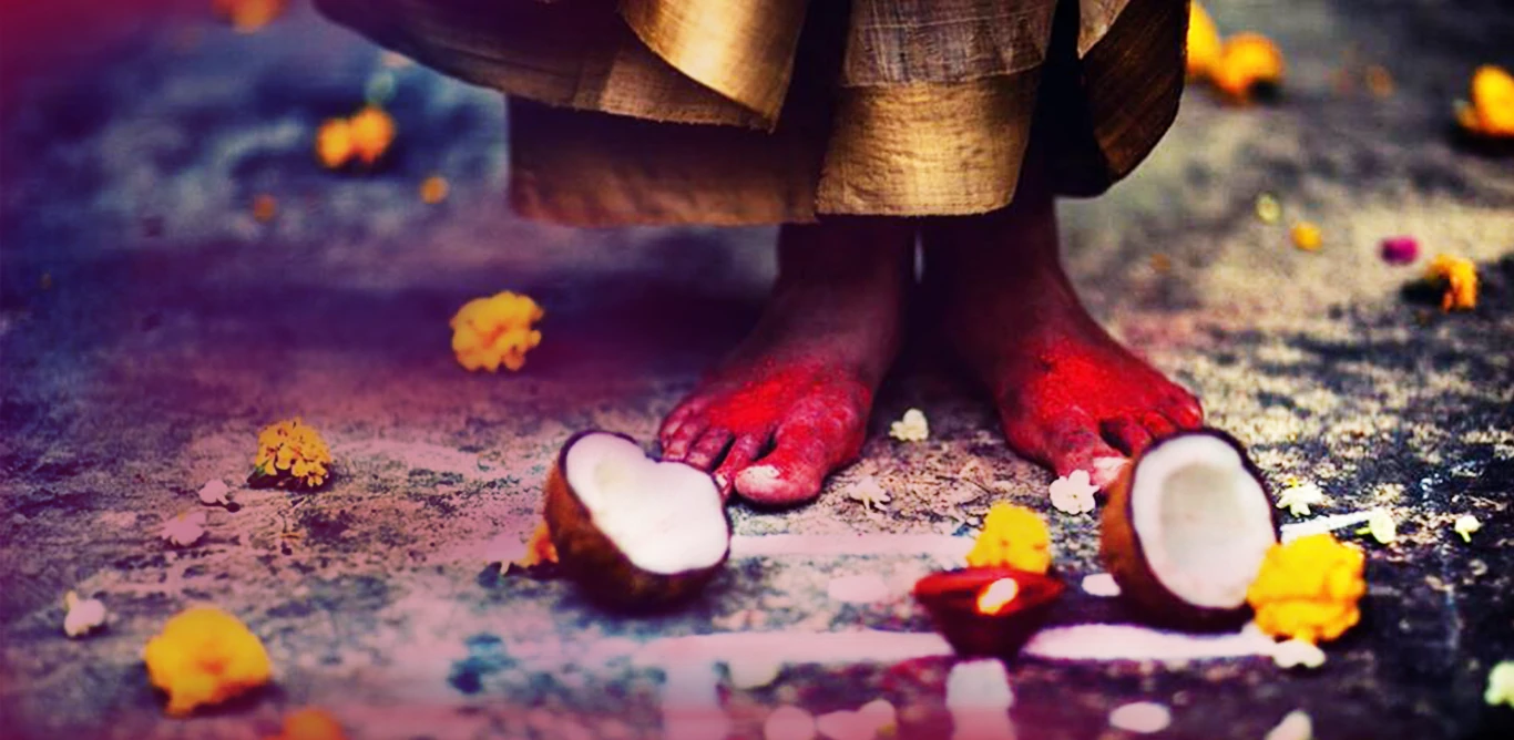 Bare feet with red alta among halved coconuts, marigolds and a diya